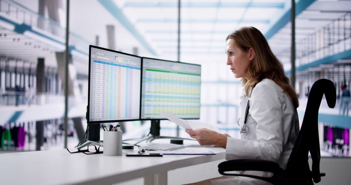 Lab administrator looking at a computer screen and holding a document in one hand
